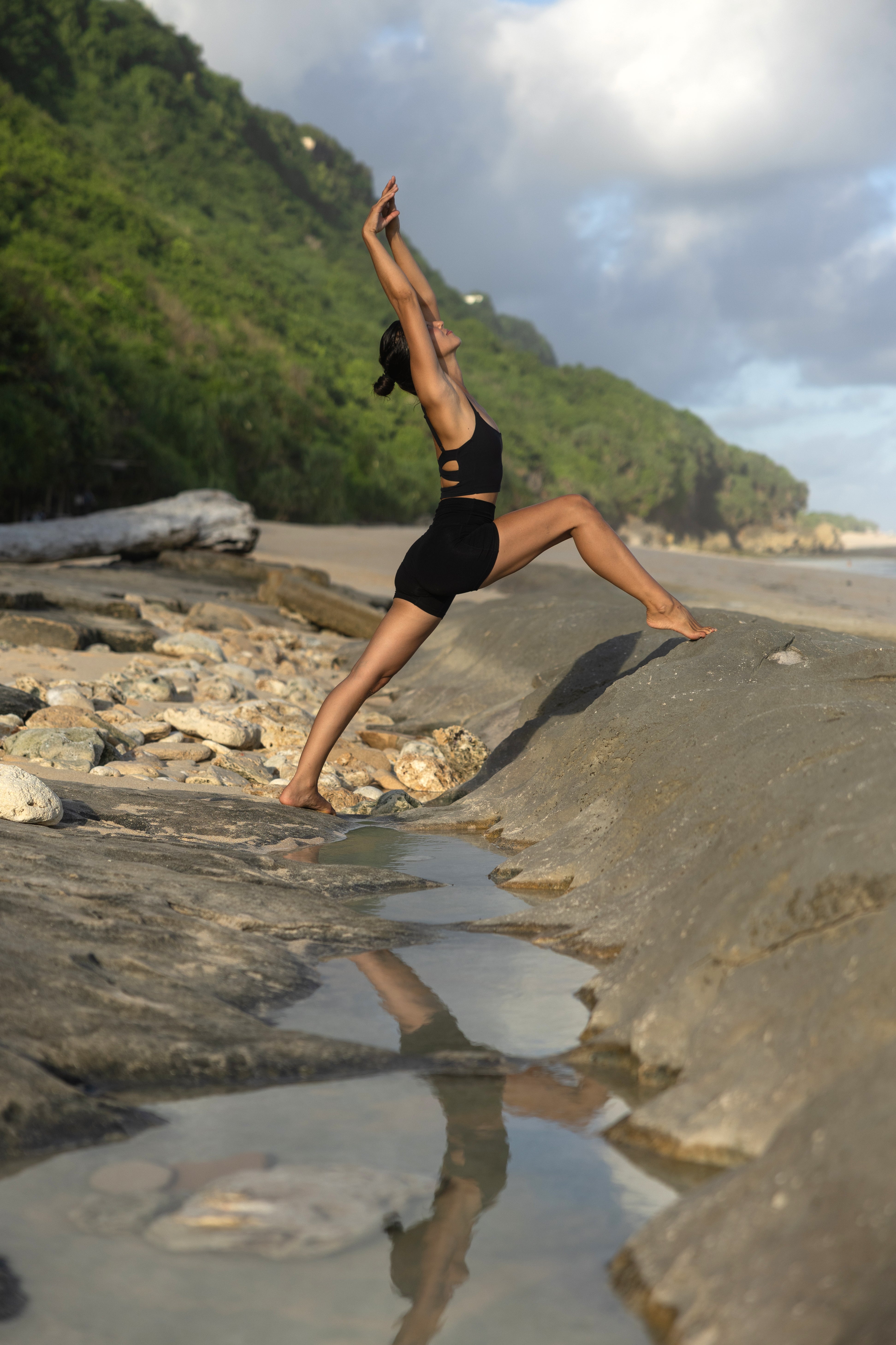 Person practicing yoga on a rocky beach with a scenic background