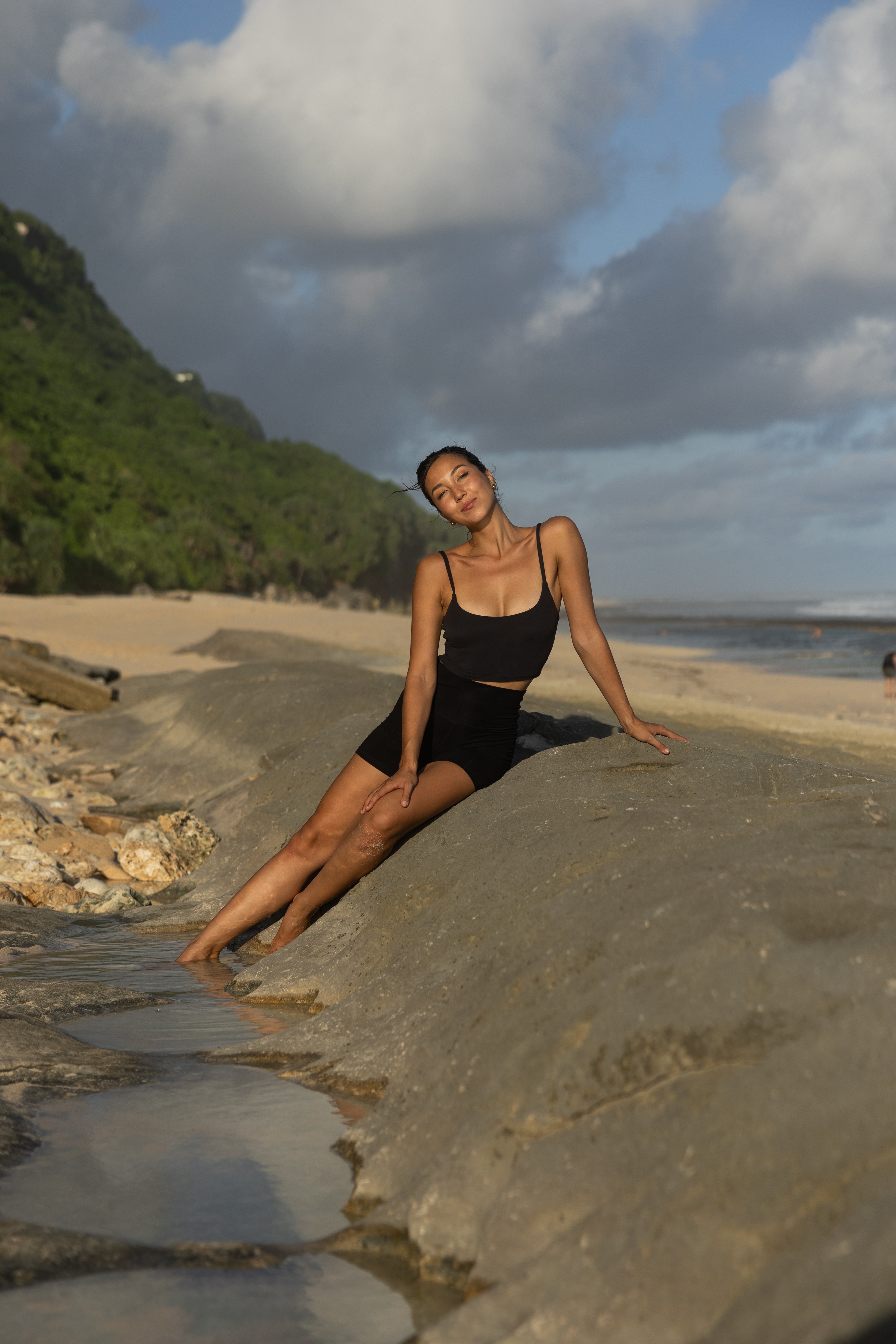 Woman in black swimsuit sitting on a rock by the beach with a scenic background