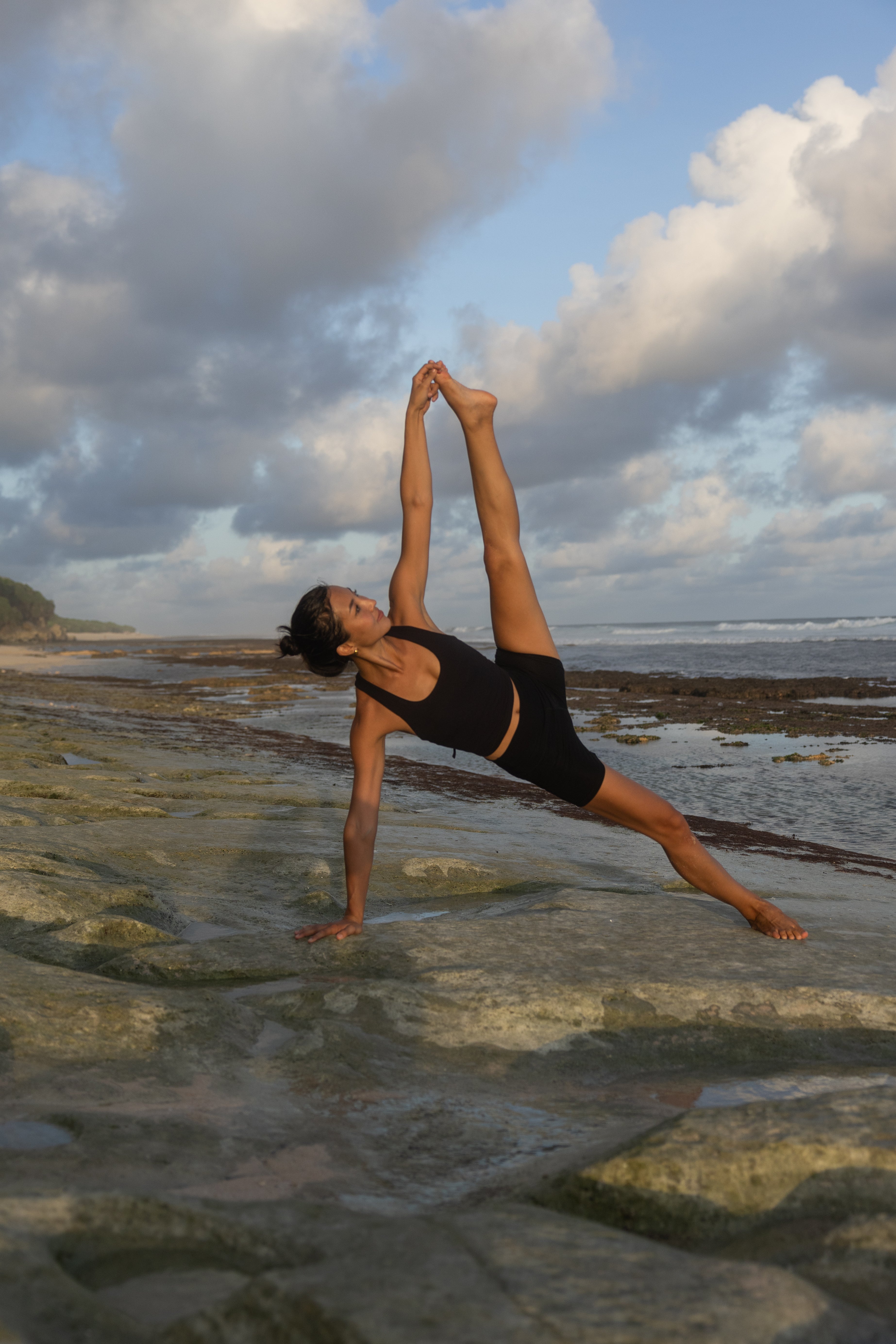 Person practicing yoga on a rocky beach with a cloudy sky