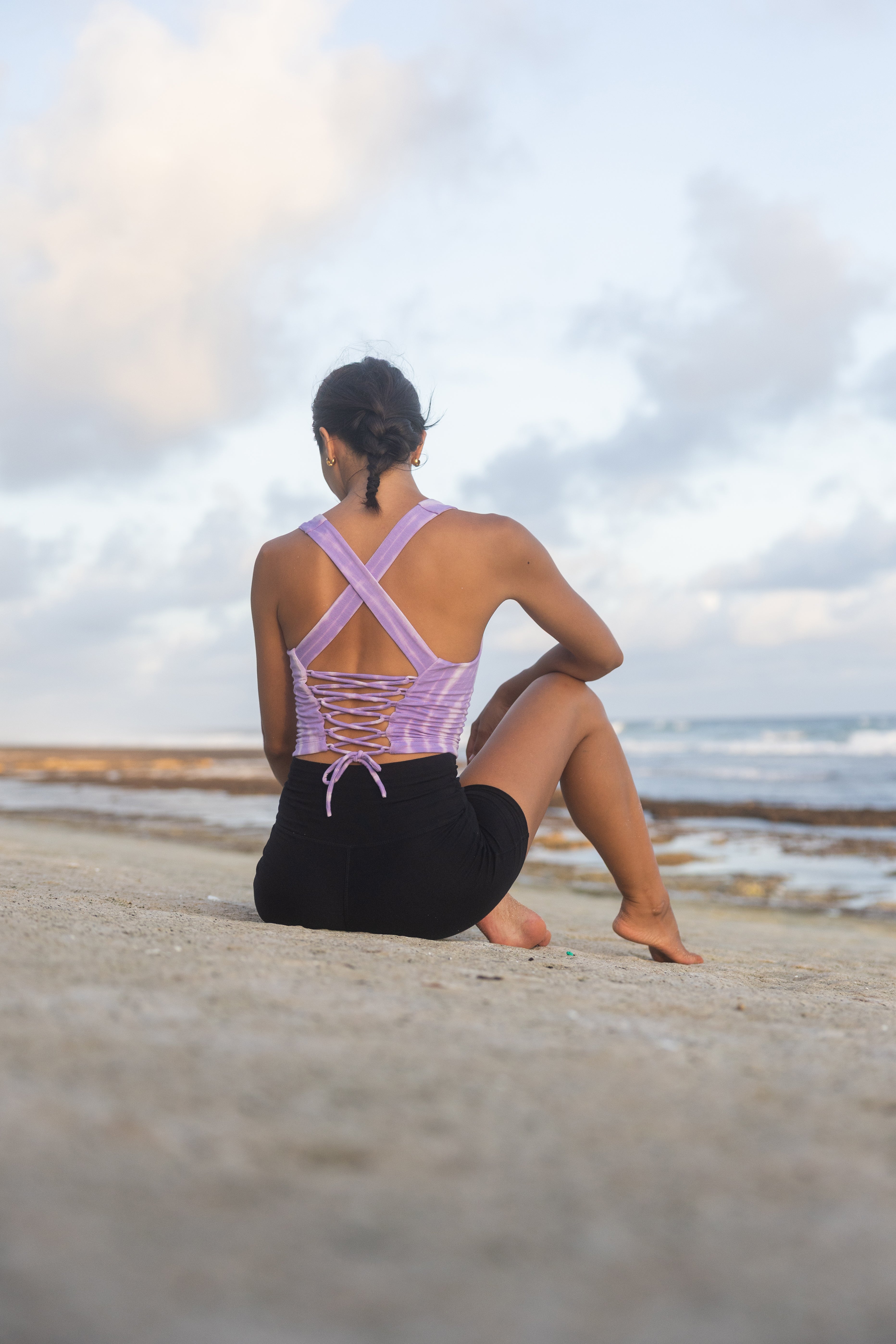 Person sitting on the beach wearing a purple top and black pants.