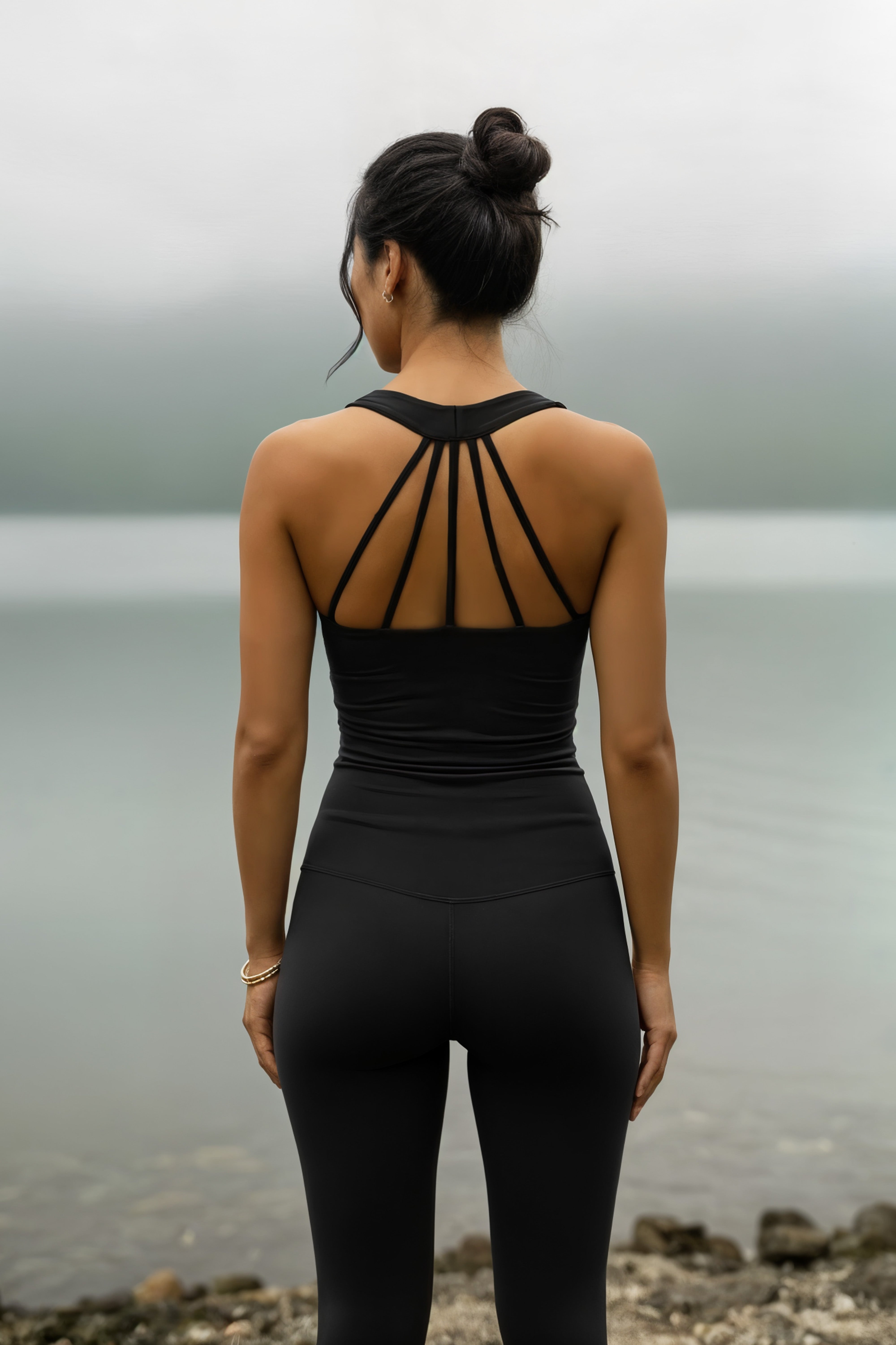Woman wearing a midnight black strappy top and leggings standing by a body of water.